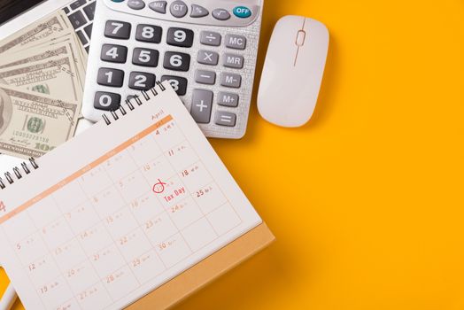April of the year is Tax Day, Top view flat lay closeup calculator, laptop computer, calendar, and Dollar money, on yellow background business finance budget concept with copy space for text