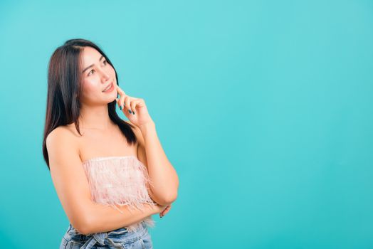 Portrait asian beautiful woman smiling her standing thinking looking out on blue background, with copy space for text