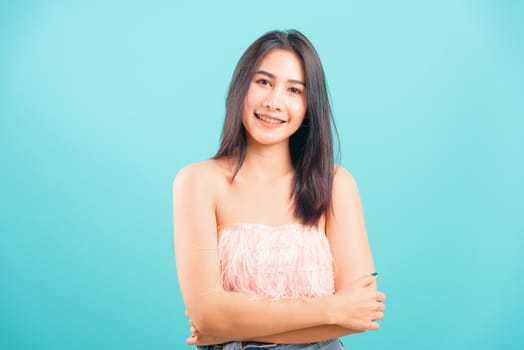 Smiling face Asian beautiful woman her cross arm looking to camera on blue background, with copy space for text