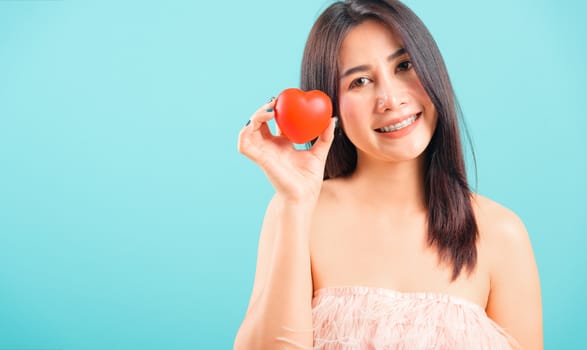 Portrait asian beautiful woman smiling her holding red heart on blue background, with copy space for text, valentine's day concept