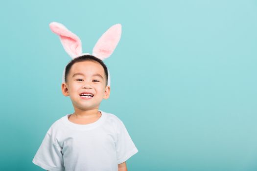 Easter day concept, Happy Asian cute little child boy smile beaming wearing bunny ears and white T-shirt standing on blue background with copy space