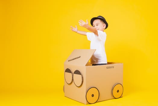 Portrait happy Asian cute little children boy smile so happy wearing white T-shirt driving car creative by cardboard, studio shot on yellow background with copy space