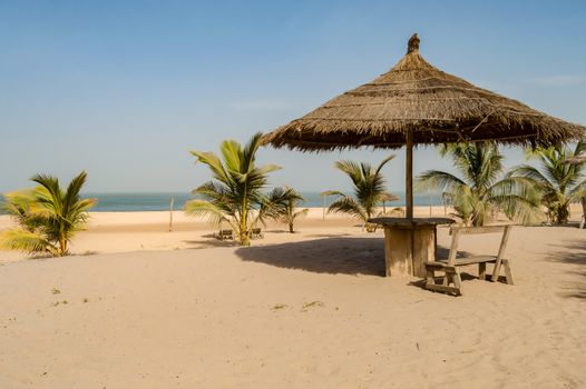 Straw umbrella with a small wooden bench and a table on Bijilo Beach in The Gambia