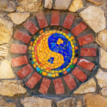 Circular mosaic religious symbol of Yin and yang on stone wall.