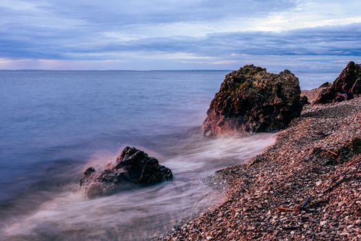 Boulders on the riverbank in sunrise light and smoothing waves