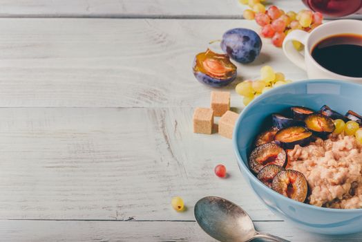 Healthy breakfast concept. Porridge with fresh plum, green grapes and cup of coffee. Ingredients over wooden background.