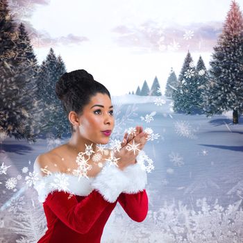 Pretty santa girl blowing over her hands against snowy landscape with fir trees
