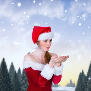 Pretty girl in santa costume holding hand out against snowy landscape with fir trees