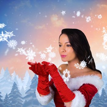 Pretty girl in santa outfit blowing against snow falling on fir tree forest