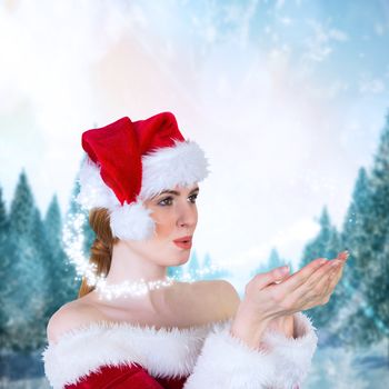 Pretty girl in santa costume holding hand out against snowy landscape with fir trees