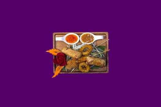 Mixed plate with thai food with purple background and copy space. Plate made out of wood and spring rolls
