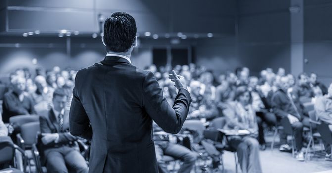 Speaker at Business Conference with Public Presentations. Audience at the conference hall. Entrepreneurship club. Rear view. Panoramic composition. Blue toned greyscale.