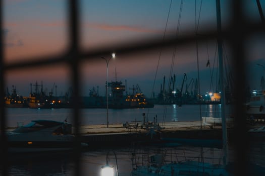 Stunning night view through a metal fence with a yacht and some ships for background.