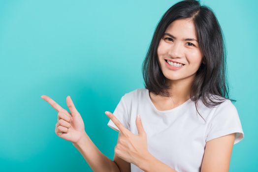 Portrait Asian beautiful young woman wearing white T-shirt standing smile white teeth, She pointing finger up and looking at camera, shoot photo in studio on blue background, There was copy space.