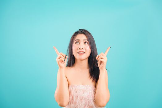Smiling face Asian beautiful woman her point up and looking up on blue background, with copy space for text