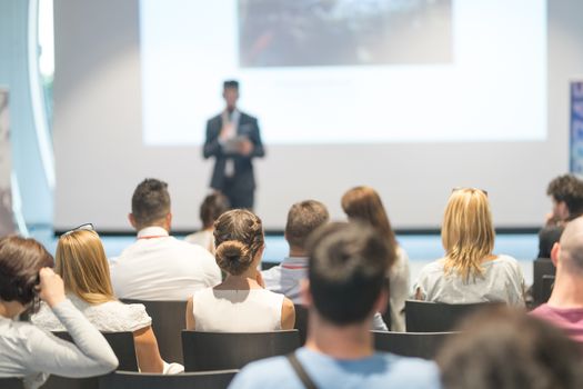 Male speaker giving a talk in conference hall at business event. Audience at the conference hall. Business and Entrepreneurship concept. Focus on unrecognizable people in audience.