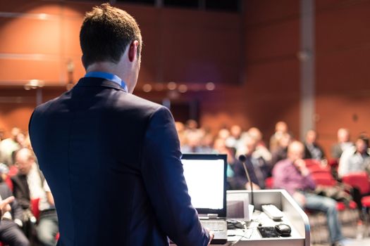 Speaker giving a talk on corporate business conference. Unrecognizable people in audience at conference hall. Business and Entrepreneurship event.