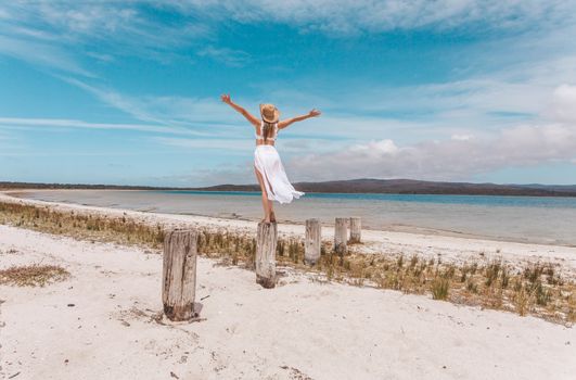 A female on vacation at the beach wearing a white swimsuit with sarong skirt,arms outstretched feeling free, alive, full of joy.  Australian travel, tourism or emotion concept