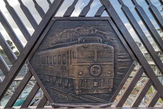 Engraving on metal representing the famous Hokutosei train on the Shimogoindenbashi Bridge that reaches the Nippori and Yanaka neighborhoods in the Arakawa district at the north exit of the Nippori Station on the JR Yamanote Line in Tokyo. In the center of the bridge is a balcony called the Train Museum which allows to observe the 2500 trains that pass each day below. The bridge dating back to the 1930s has been renovated several times to adapt to the evolution of traffic and was completed in its current form in 1988.
