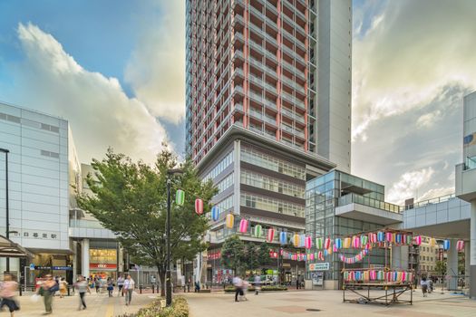 View of the square in front of the Nippori train station decorated for the Obon festival in the sunset summer sky with a yagura tower and paper lanterns in the Arakawa district of Tokyo.