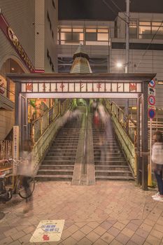 Illuminated metal portal decorated with maple leaves and a capital at the bottom of the stairs of the Momiji Bridge at Nippori Station close to the Nippori Fabric Town in the Arakawa district of Tokyo, Japan.