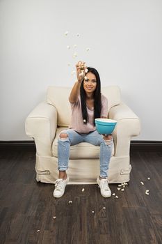 Young woman, sitting on a couch, throwing popcorn