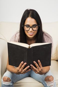 young woman sitting on a couch, wearing glasses, reading a book