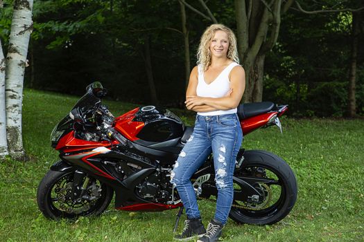 Twenty something woman, in a park, standing in front of a sport motocycle