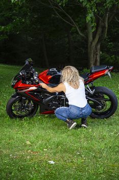 young woman, wearing a white tank top and jeans, working on a sport motocycle