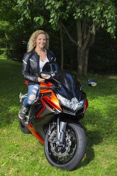 Blond woman, in her twenties, sitting on top of a sport motocycle, in a park