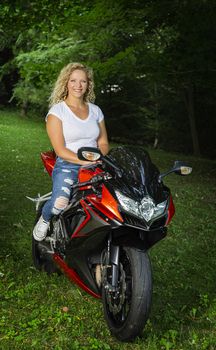 Young blond woman, wearing a white t-shirt and ripped jean, sitting on a sport motocycle