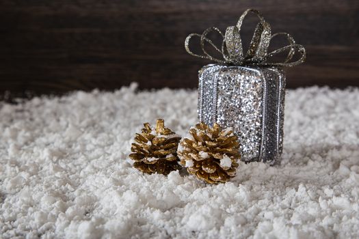 small silver gift and two gold pine cone on snow against dark wood background