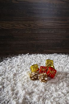 Large view of gold and red present with two gold pine cone in the snow against a dark wood background