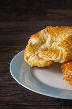 Close up of a croissant on a blue rimmed plate against a dark wood background