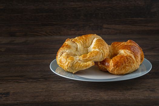 two croissant, stake on top of one another, on a blue rimmed plate against a dark wood background