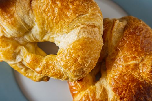 close up view of two croissants stake on top of one another on a blue rimmed plate