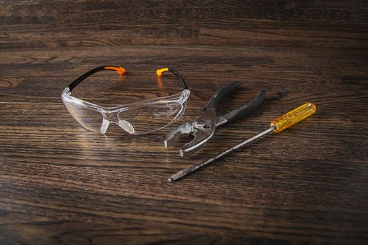 protective glasses, plier and screwdrive on a dark wood background
