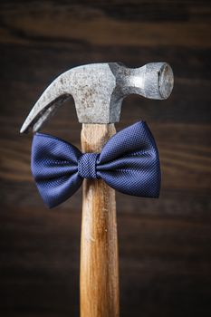 Old weather hammer wearing a blue bowtie against a dark wood background