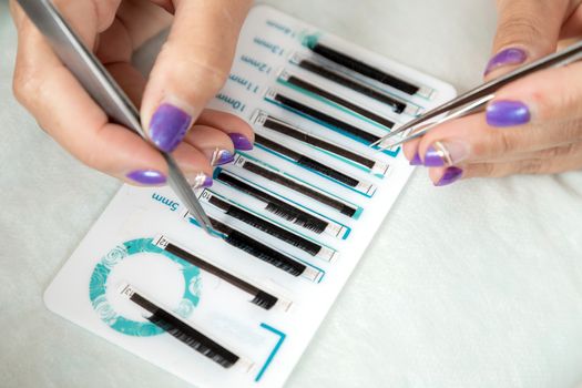 master lash maker is holding one false eyelash by tweezers in hand, close-up