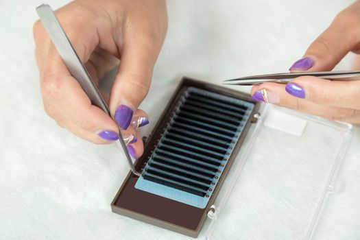 master lash maker is holding one false eyelash by tweezers in hand, close-up