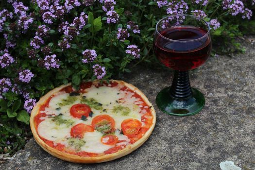 The picture shows pizza and red wine on blossoming thyme