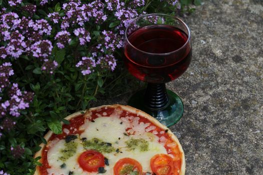 The picture shows pizza and red wine on blossoming thyme