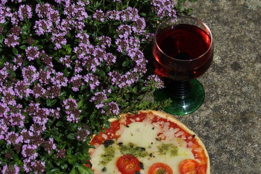 The picture shows pizza and red wine on blossoming thyme