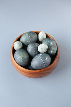 Creatively painted chicken and quail Easter eggs with natural hibiscus dye, look like sea stones in bowl on gray background, copy space. Happy Easter DIY concept. Soft selective focus. Flat lay.