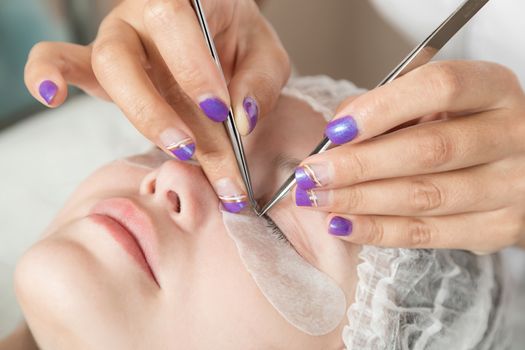 master is performing procedure of lash extension on female eyelids in a beauty salon