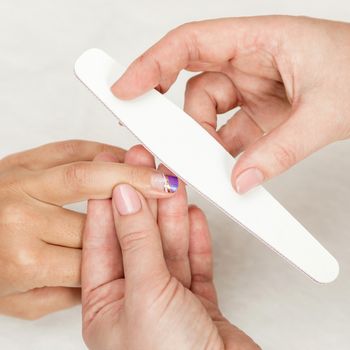 Woman in a nail salon receiving a manicure by a beautician with nail file. Nails manicure.