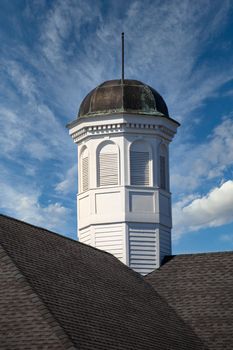 A white wood cupola on a grey shingled roof with tarnished copper top under clear blue skies