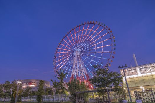 Odaiba colorful tall Palette Town Ferris wheel named Daikanransha visible from the central urban area of Tokyo in the summer sunset purple blue sky. Passengers can see the Tokyo Tower, the twin-deck Rainbow Bridge, and Haneda Airport, as well as central Tokyo during their ride.