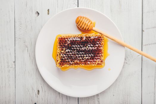 Top view of delicious yummy honeycomb on bright plate with honey dipper over light wooden background