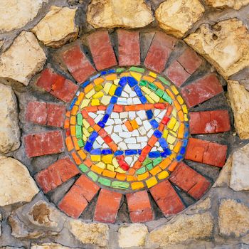 Circular mosaic religious symbol Star of David on stone wall.